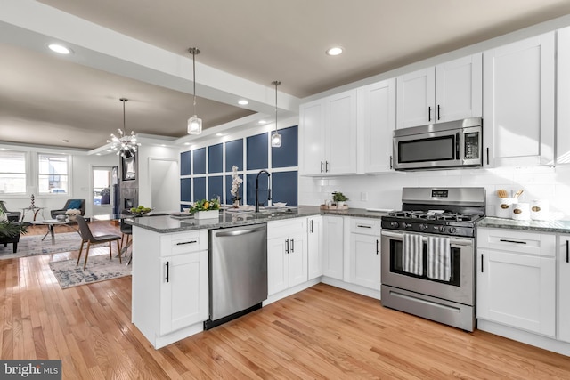 kitchen with hanging light fixtures, appliances with stainless steel finishes, light wood-type flooring, and white cabinetry