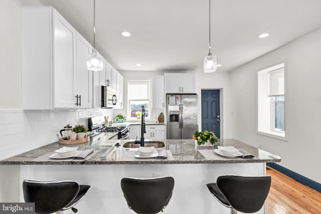 kitchen featuring a breakfast bar area, sink, kitchen peninsula, appliances with stainless steel finishes, and white cabinetry