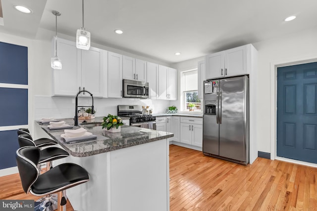 kitchen featuring light hardwood / wood-style floors, pendant lighting, stainless steel appliances, kitchen peninsula, and white cabinetry