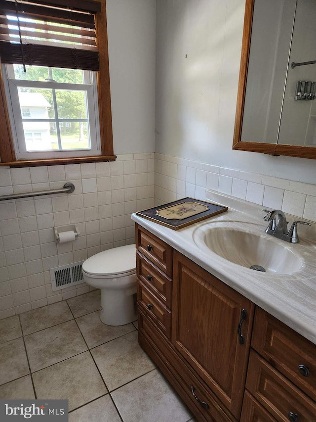 bathroom with toilet, vanity, tile patterned floors, and tile walls