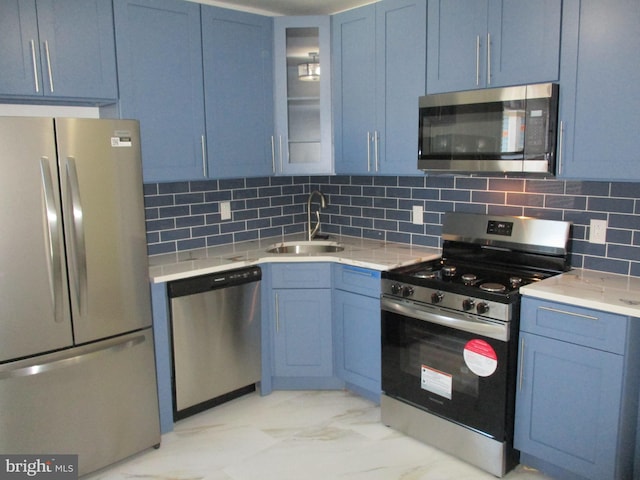 kitchen with stainless steel appliances, decorative backsplash, sink, blue cabinetry, and light stone countertops