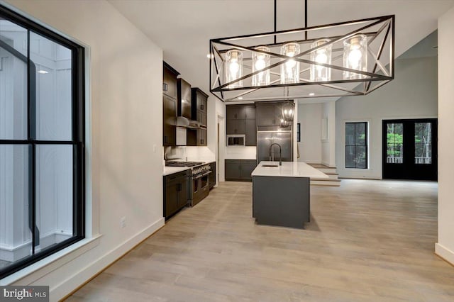 kitchen featuring dark brown cabinets, light wood-type flooring, decorative light fixtures, and an island with sink