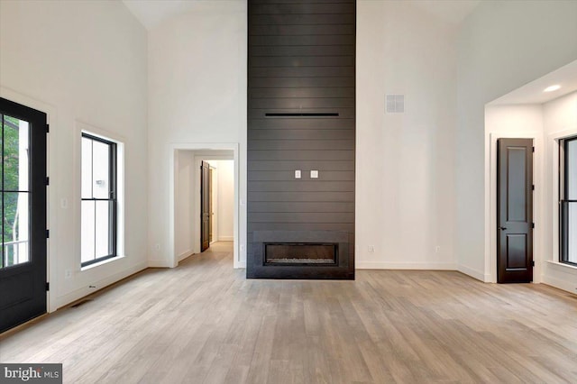 unfurnished living room featuring a large fireplace, a towering ceiling, and light hardwood / wood-style floors