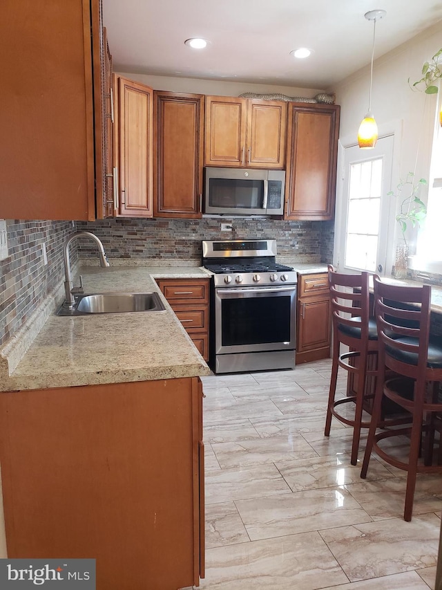 kitchen with backsplash, brown cabinetry, stainless steel appliances, a sink, and hanging light fixtures