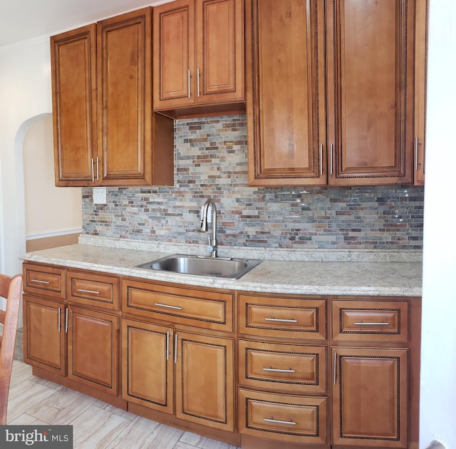 kitchen featuring brown cabinets, decorative backsplash, a sink, and light stone countertops