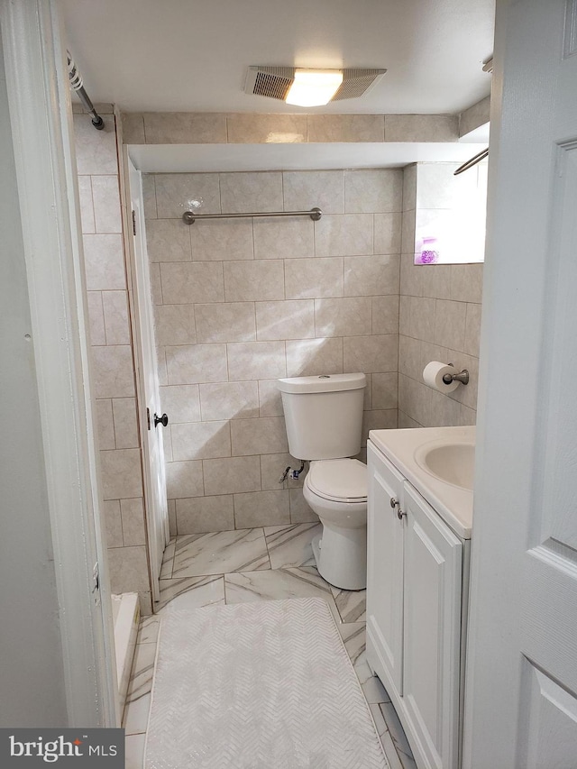 bathroom with tile walls, a tile shower, vanity, and toilet