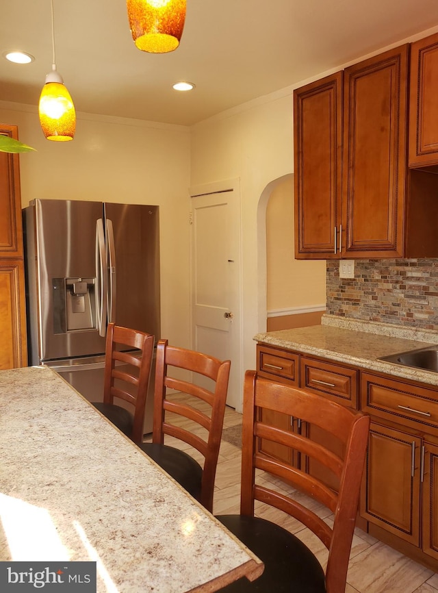 kitchen featuring light stone countertops, decorative light fixtures, stainless steel fridge with ice dispenser, and decorative backsplash