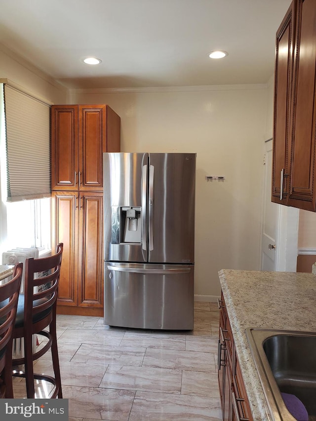 kitchen with stainless steel fridge with ice dispenser, crown molding, sink, and light stone countertops