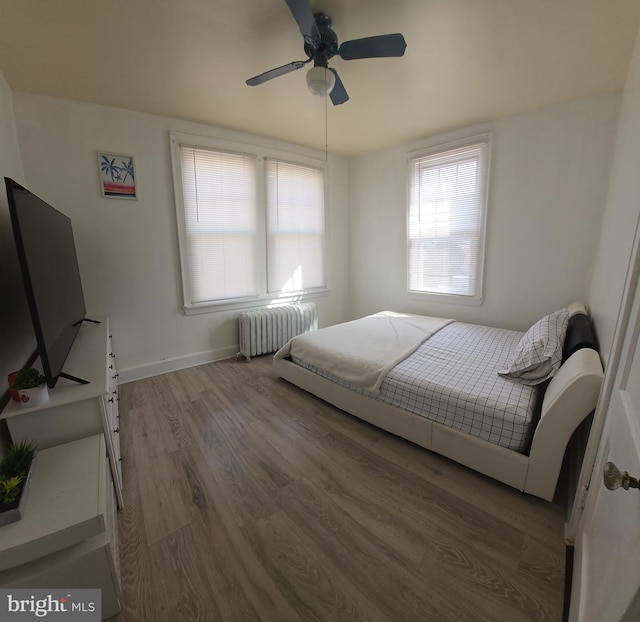 bedroom featuring radiator, wood finished floors, baseboards, and a ceiling fan