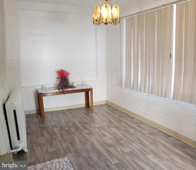 unfurnished dining area featuring radiator heating unit, wood finished floors, brick wall, a notable chandelier, and baseboards