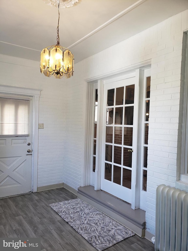 interior space featuring dark wood-type flooring, brick wall, an inviting chandelier, and radiator