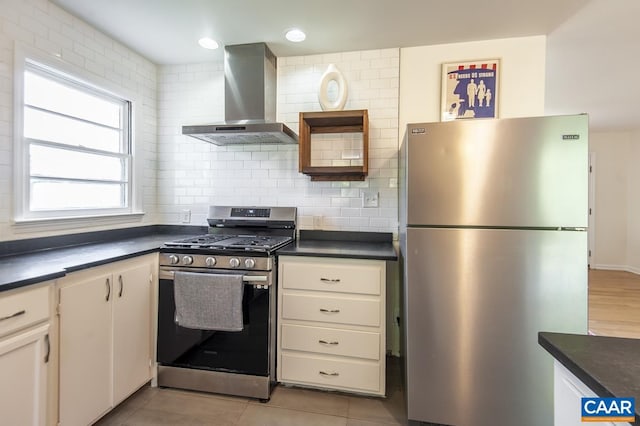 kitchen featuring light tile patterned flooring, wall chimney exhaust hood, backsplash, white cabinetry, and stainless steel appliances