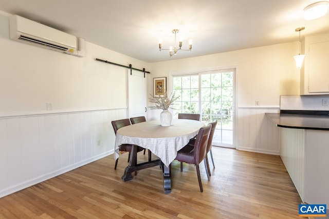 dining space featuring light hardwood / wood-style flooring, a chandelier, a barn door, and a wall unit AC