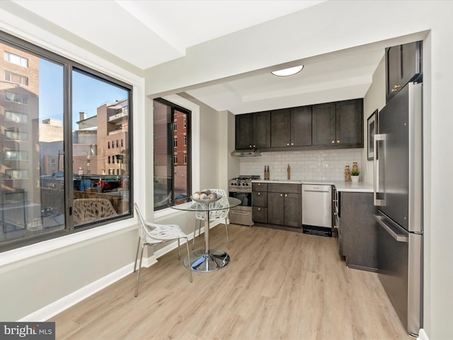 kitchen with dark brown cabinetry, stainless steel appliances, light countertops, light wood-type flooring, and backsplash