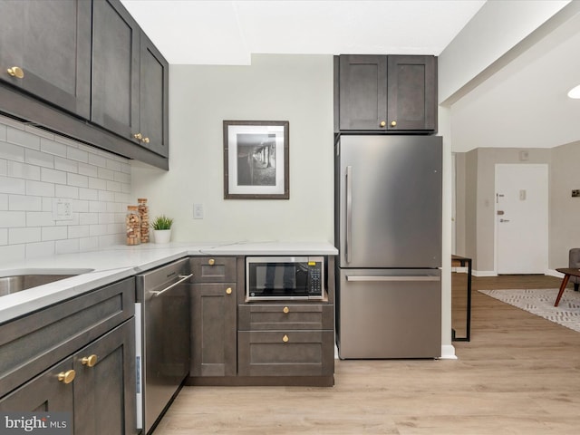 kitchen with decorative backsplash, dark brown cabinets, light stone counters, light hardwood / wood-style flooring, and stainless steel appliances