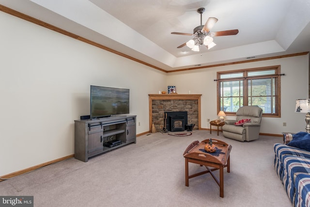 living room featuring a raised ceiling, a wood stove, carpet floors, ceiling fan, and ornamental molding