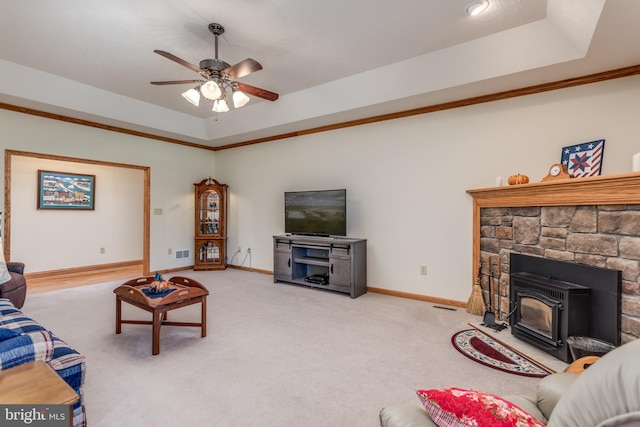 carpeted living room with ceiling fan, a raised ceiling, a wood stove, and ornamental molding