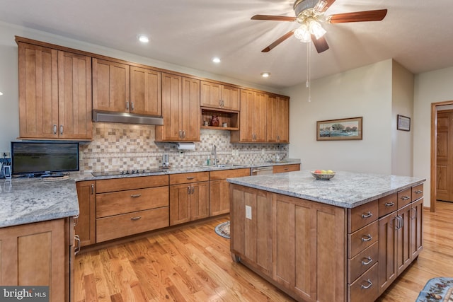 kitchen featuring black electric stovetop, light hardwood / wood-style floors, light stone countertops, and sink