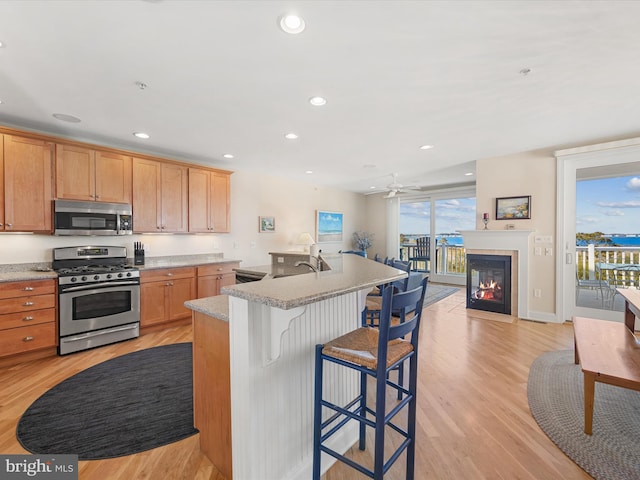 kitchen featuring ceiling fan, appliances with stainless steel finishes, a kitchen island with sink, a kitchen bar, and light hardwood / wood-style floors