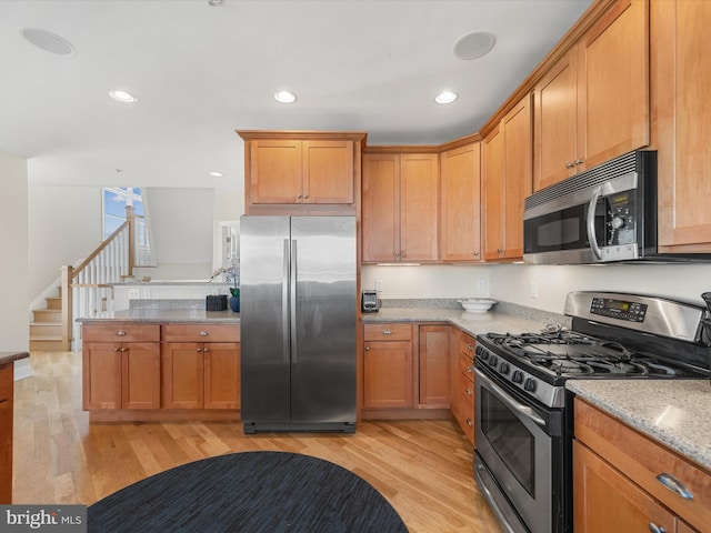 kitchen featuring light stone countertops, appliances with stainless steel finishes, and light wood-type flooring