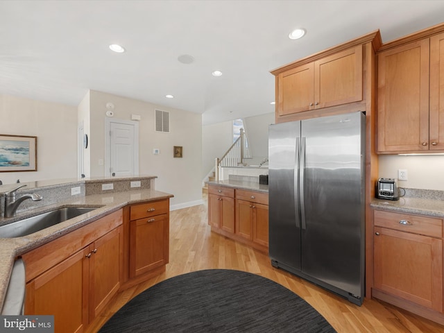 kitchen featuring stainless steel fridge, light stone countertops, light hardwood / wood-style flooring, dishwasher, and sink