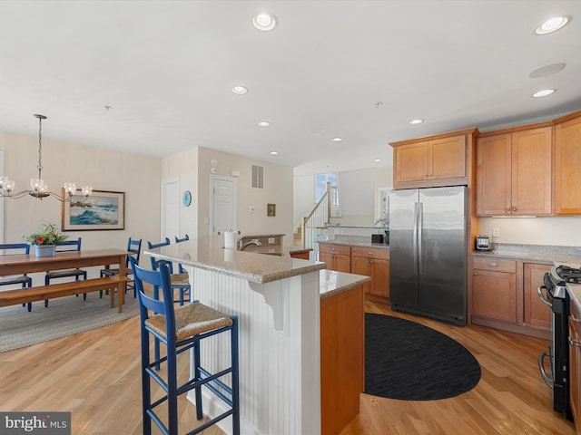 kitchen featuring light stone counters, appliances with stainless steel finishes, light hardwood / wood-style flooring, and an island with sink