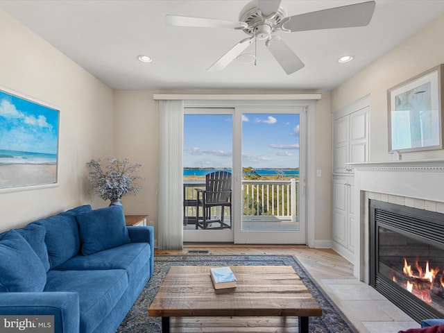 living room with a tiled fireplace, light wood-type flooring, and ceiling fan