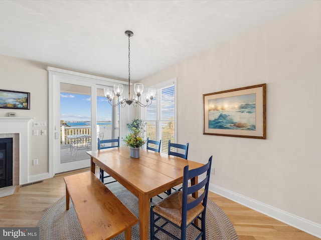 dining room featuring light hardwood / wood-style flooring, a tiled fireplace, and a notable chandelier