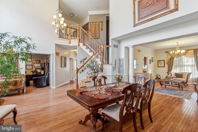 dining space featuring a towering ceiling, decorative columns, crown molding, light hardwood / wood-style flooring, and a chandelier