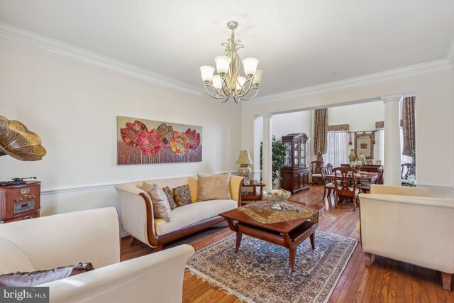 living room featuring ornamental molding, a notable chandelier, hardwood / wood-style floors, and ornate columns