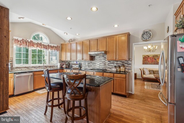 kitchen with lofted ceiling, tasteful backsplash, a kitchen island, appliances with stainless steel finishes, and light hardwood / wood-style floors