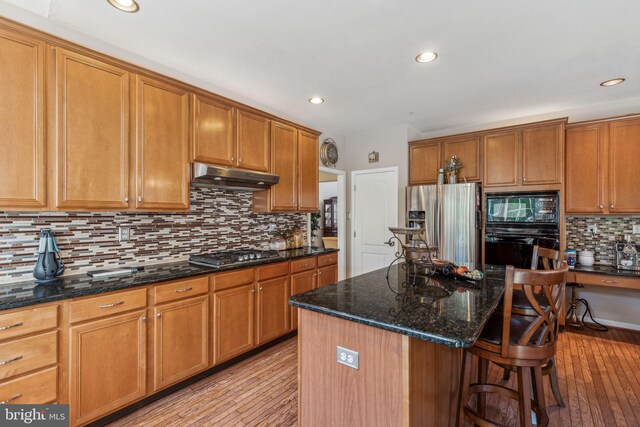 kitchen with a center island, dark stone counters, black appliances, and light wood-type flooring