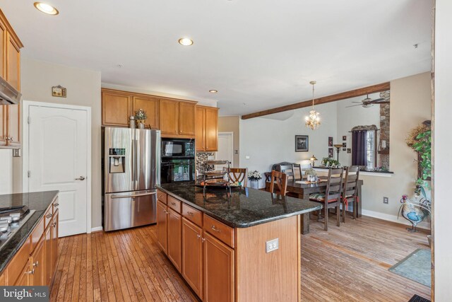 kitchen with black appliances, light wood-type flooring, ceiling fan with notable chandelier, a center island, and decorative light fixtures