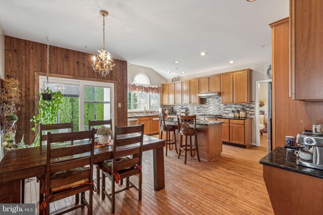 dining area with sink, light hardwood / wood-style flooring, a notable chandelier, and wood walls