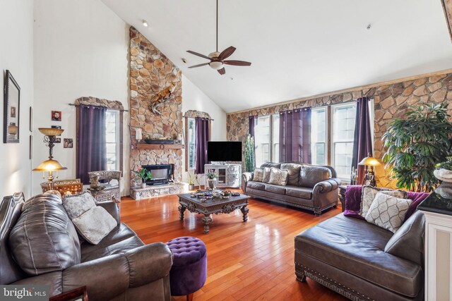 living room with a stone fireplace, hardwood / wood-style flooring, high vaulted ceiling, and ceiling fan