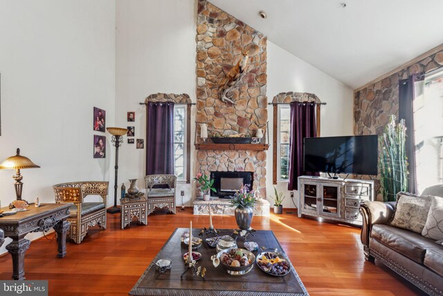 living room featuring a stone fireplace, hardwood / wood-style flooring, and high vaulted ceiling