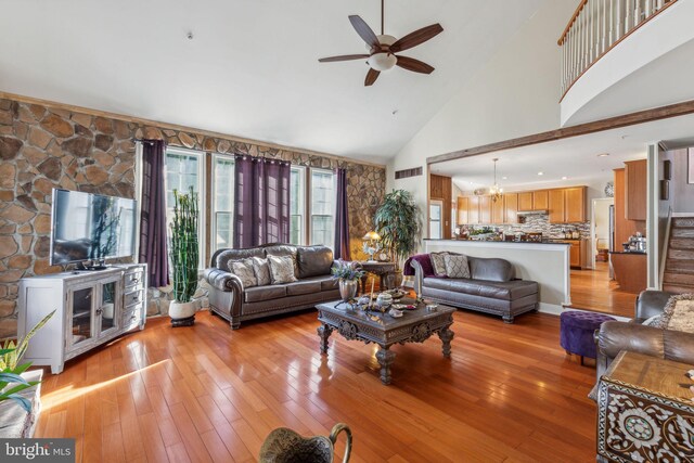 living room with high vaulted ceiling, light wood-type flooring, and ceiling fan with notable chandelier