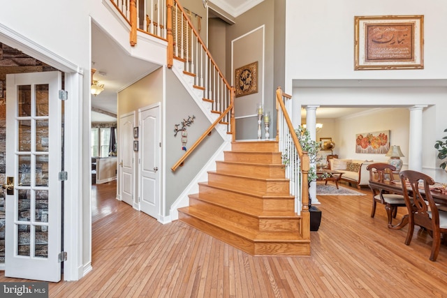 stairs with ornate columns, hardwood / wood-style flooring, a high ceiling, and crown molding