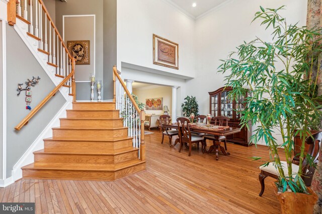 stairs featuring a towering ceiling, ornamental molding, and hardwood / wood-style flooring