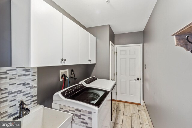 washroom with sink, light hardwood / wood-style flooring, washing machine and dryer, and cabinets