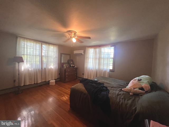 bedroom with a textured ceiling, an AC wall unit, wood-type flooring, and ceiling fan