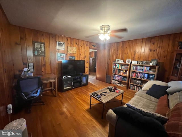 living room with ceiling fan, wood walls, and wood-type flooring