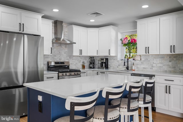 kitchen with wall chimney range hood, white cabinetry, stainless steel appliances, sink, and a center island