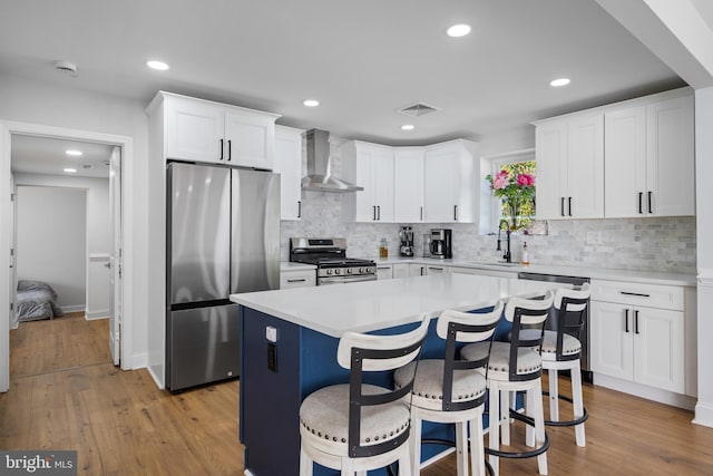 kitchen with wall chimney range hood, stainless steel appliances, sink, a center island, and white cabinets