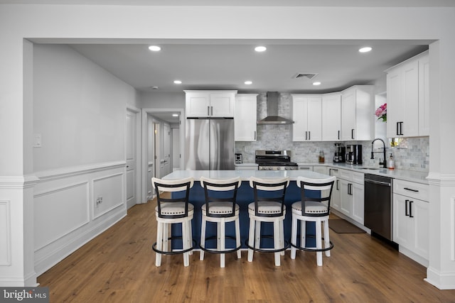 kitchen with a kitchen island, wall chimney exhaust hood, stainless steel appliances, white cabinetry, and dark hardwood / wood-style flooring