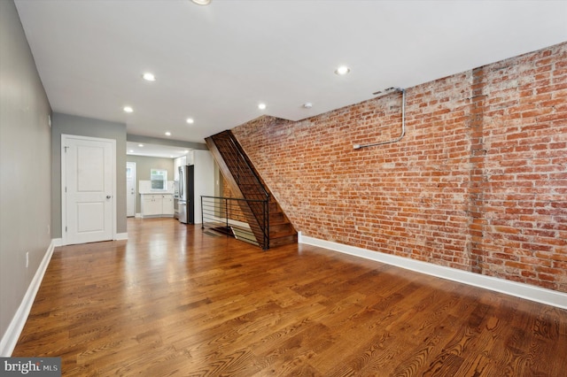 unfurnished living room featuring hardwood / wood-style flooring and brick wall