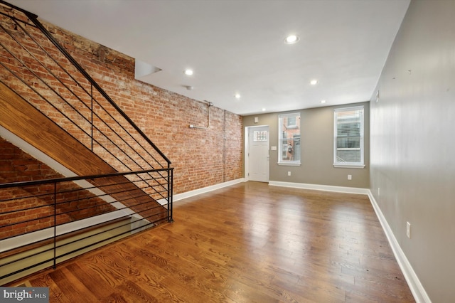 unfurnished living room with wood-type flooring and brick wall