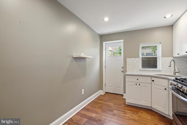 kitchen with decorative backsplash, sink, light hardwood / wood-style flooring, and white cabinetry