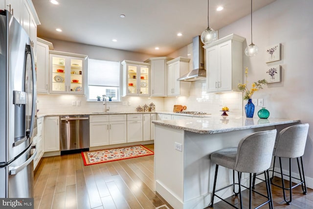 kitchen with white cabinets, pendant lighting, wood-type flooring, wall chimney range hood, and appliances with stainless steel finishes