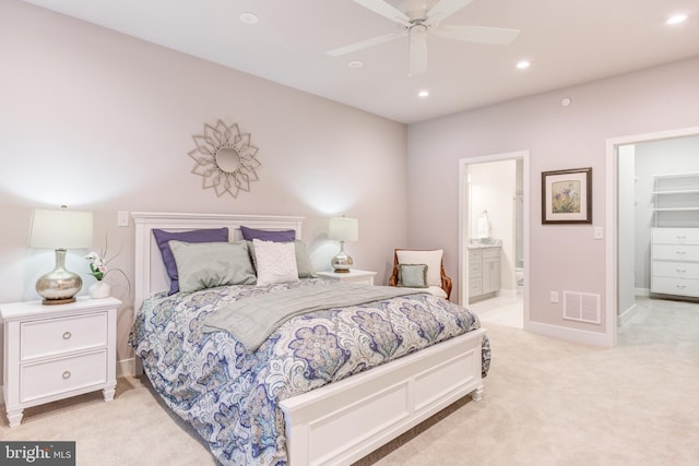 bedroom with ensuite bathroom, a spacious closet, ceiling fan, and light carpet